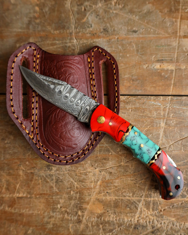 Decorative knife with turquoise handle and red sheath on a wooden surface