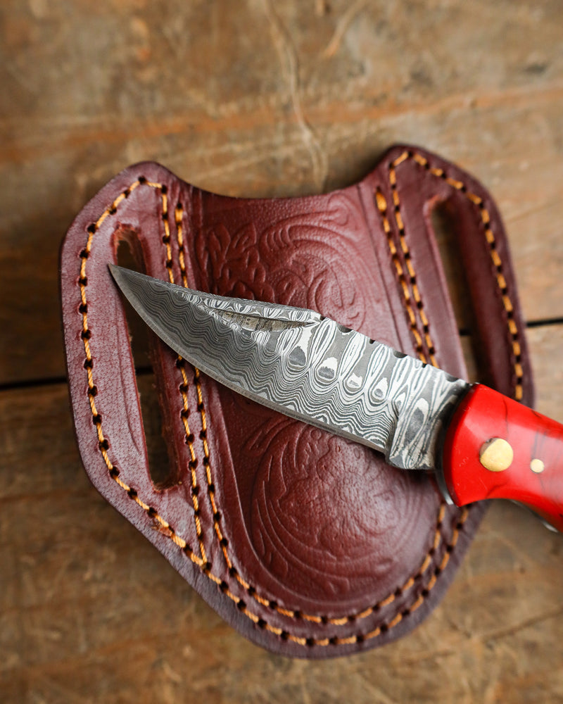 Knife with a red handle in a brown leather sheath on a wooden surface