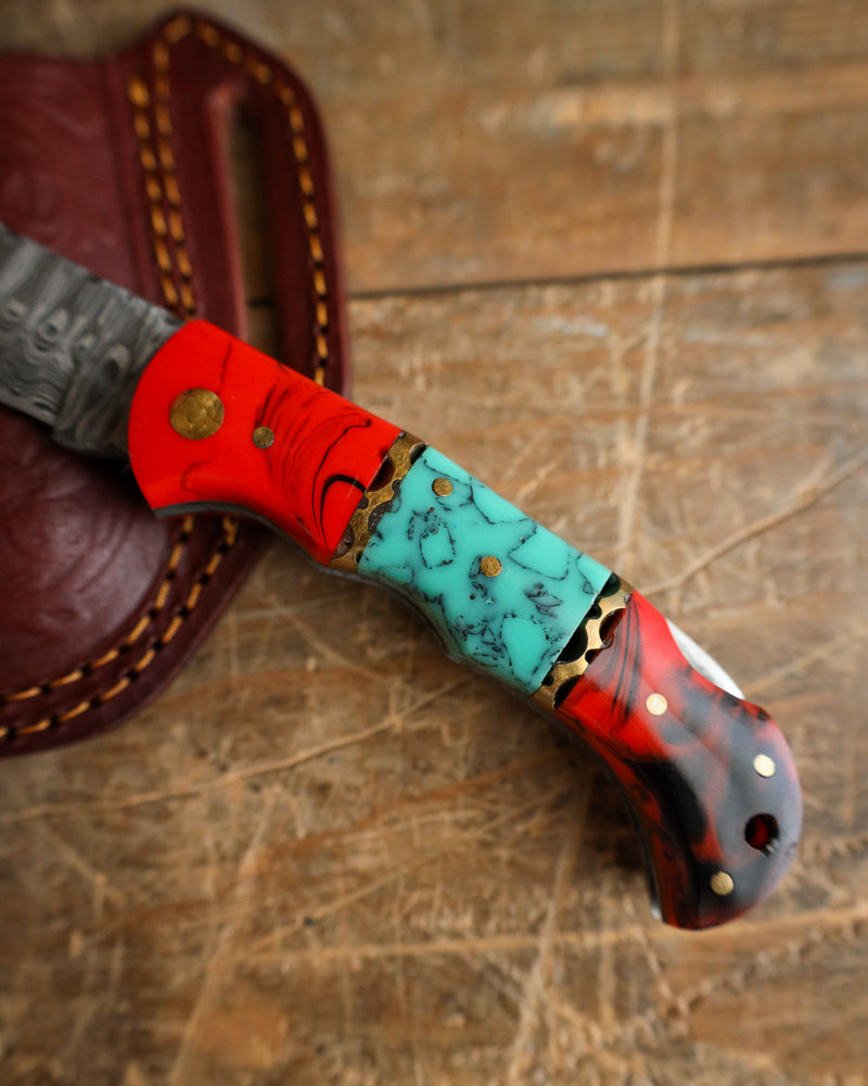 Decorative knife with a red and turquoise handle on a wooden surface