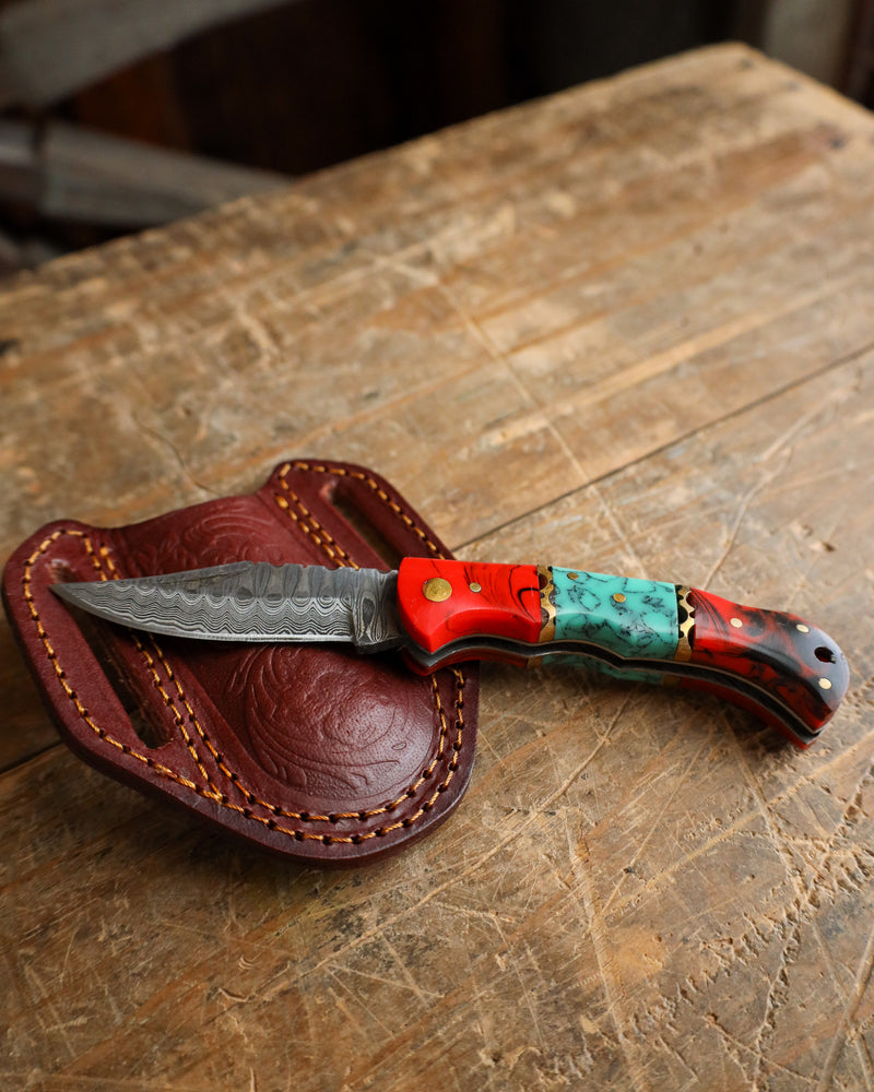 Decorative knife with a red and turquoise handle on a wooden surface
