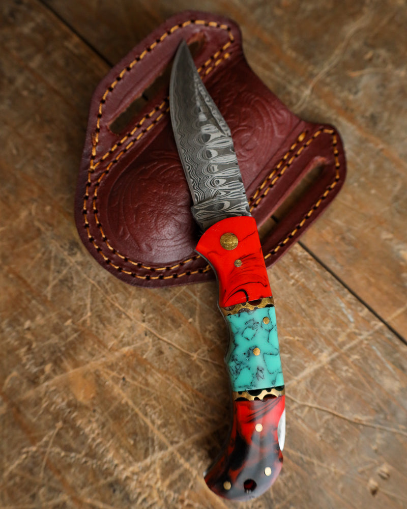 Knife with a colorful handle and red sheath on a wooden surface