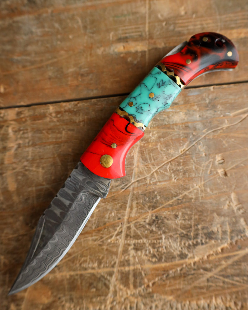Decorative knife with a red and turquoise handle on a wooden surface