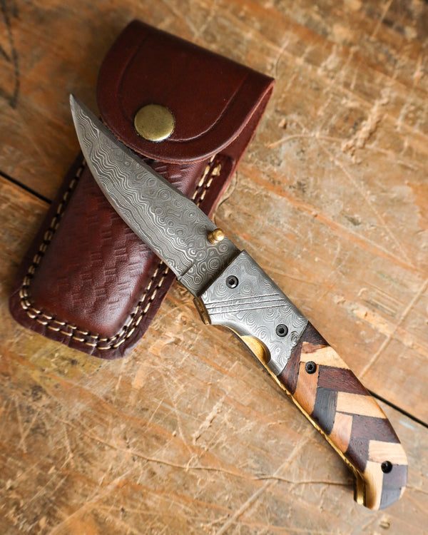 Forked blade knife with wooden handle in a leather sheath on a wooden surface