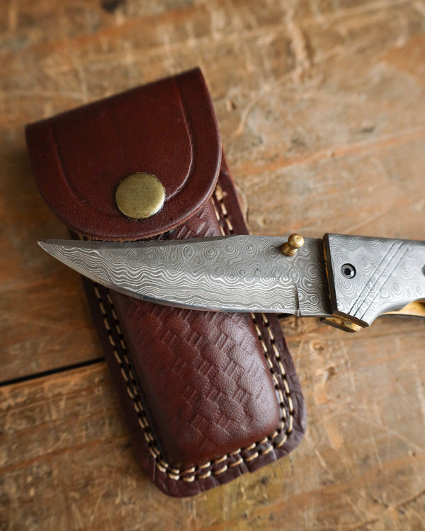 Decorative knife with a brown leather sheath on a wooden surface