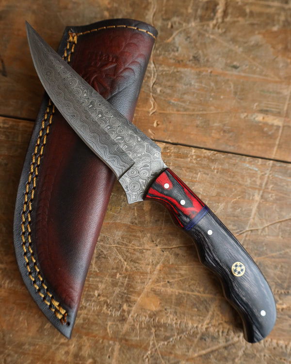 Decorative knife with a black and red handle in a leather sheath on a wooden surface