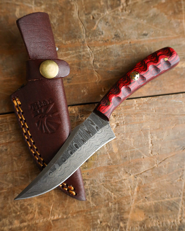 Knife with red handle and brown leather sheath on a wooden surface