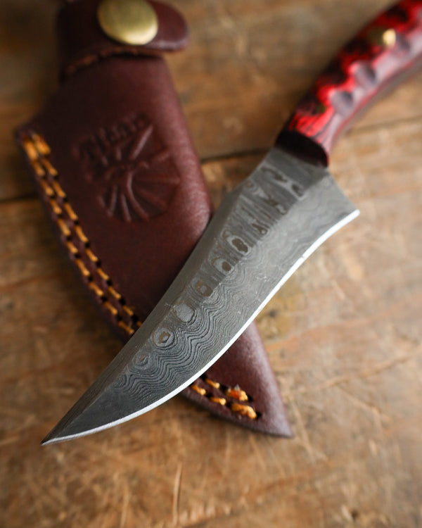 Knife with a red handle and leather sheath on a wooden surface