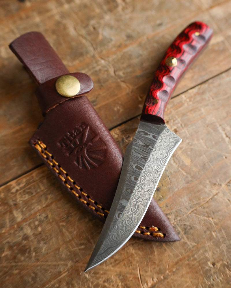 Knife with red handle and brown leather sheath on a wooden surface