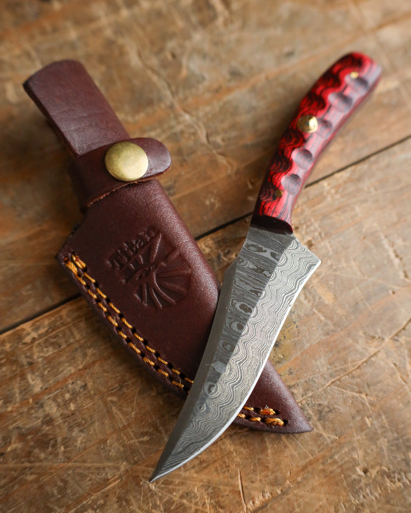 Knife with red handle and brown leather sheath on a wooden surface