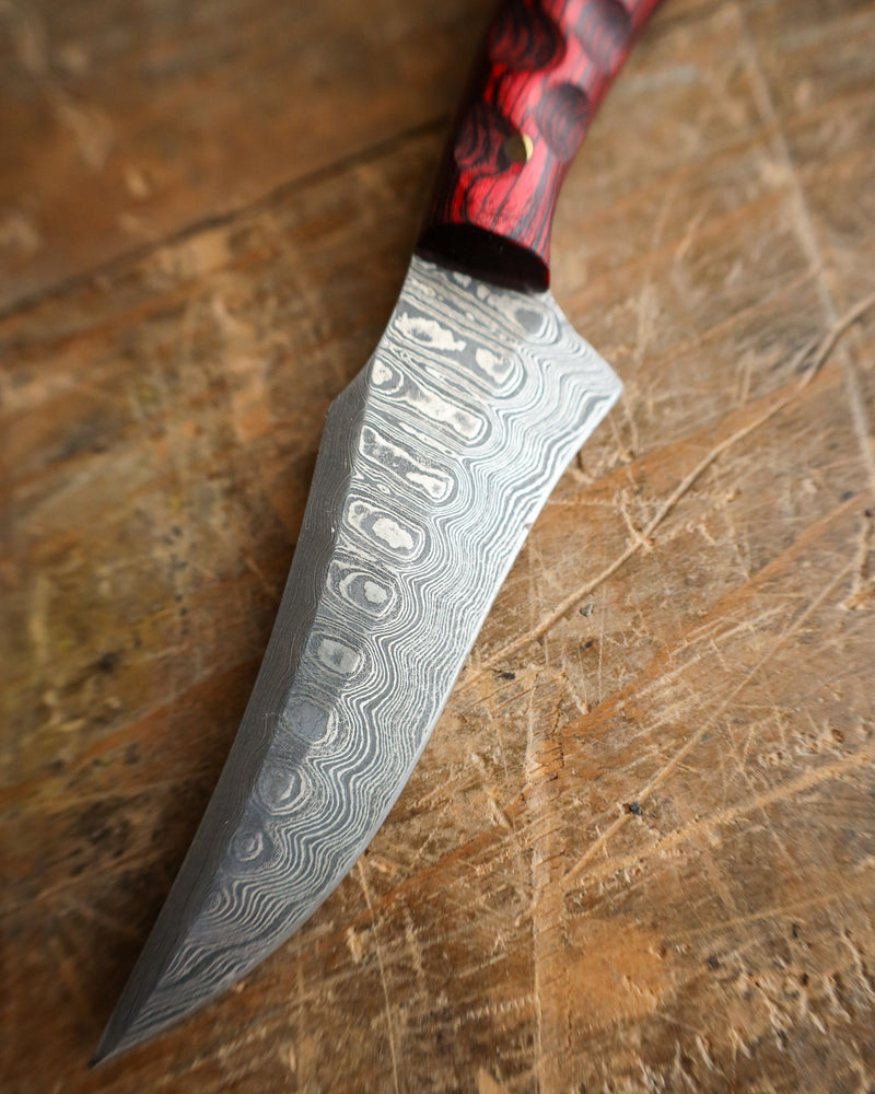 Damascus knife with a red and black handle on a wooden surface