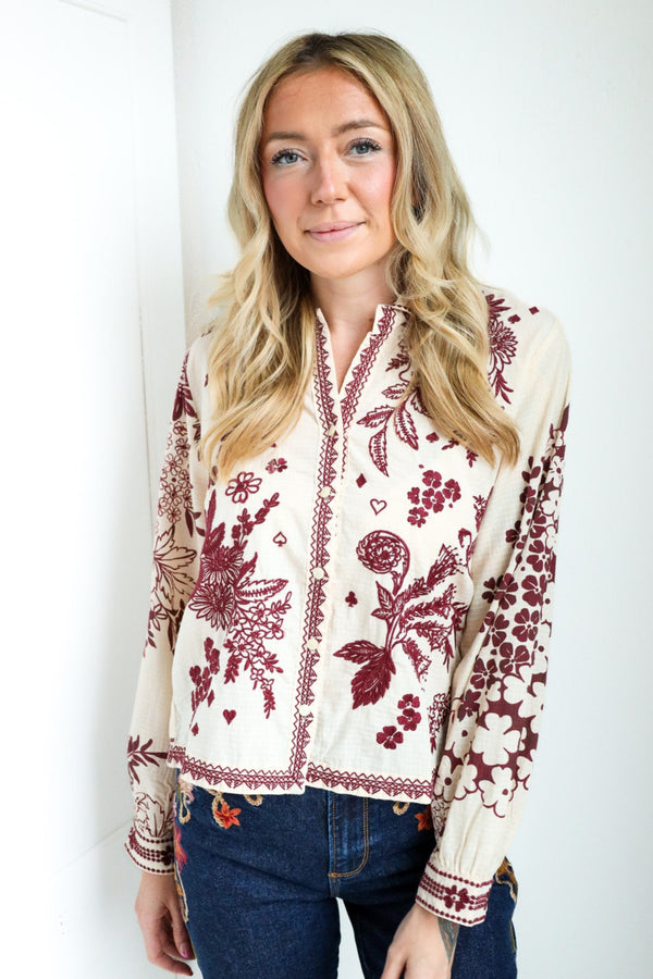 Woman wearing a white blouse with red floral patterns against a white background
