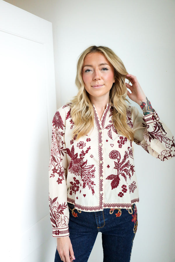 Woman wearing a white blouse with red floral patterns against a plain background