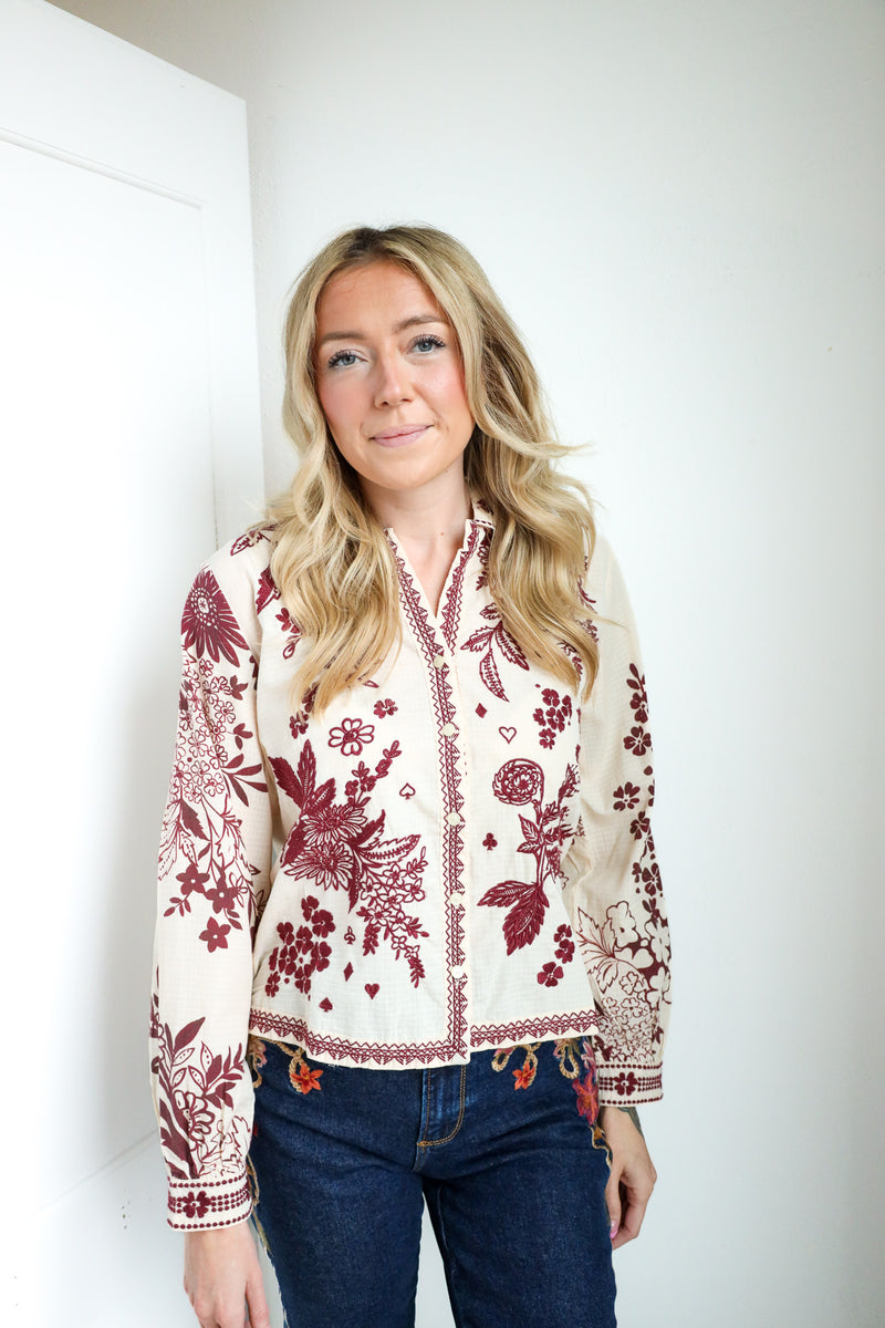Woman wearing a white blouse with red floral patterns against a white background