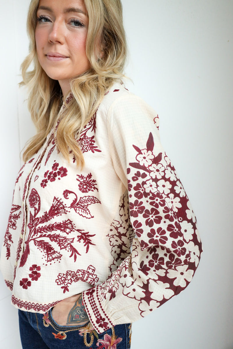 Woman wearing a white blouse with red floral embroidery on a plain background
