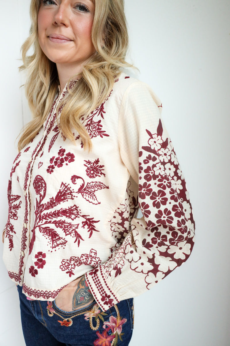 Woman wearing a cream blouse with red floral embroidery on a white background