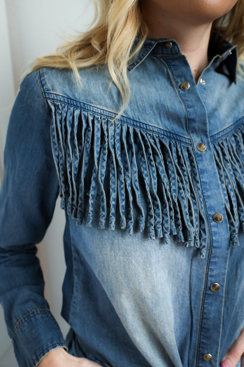 Blue denim shirt with fringe details worn by a person against a neutral background