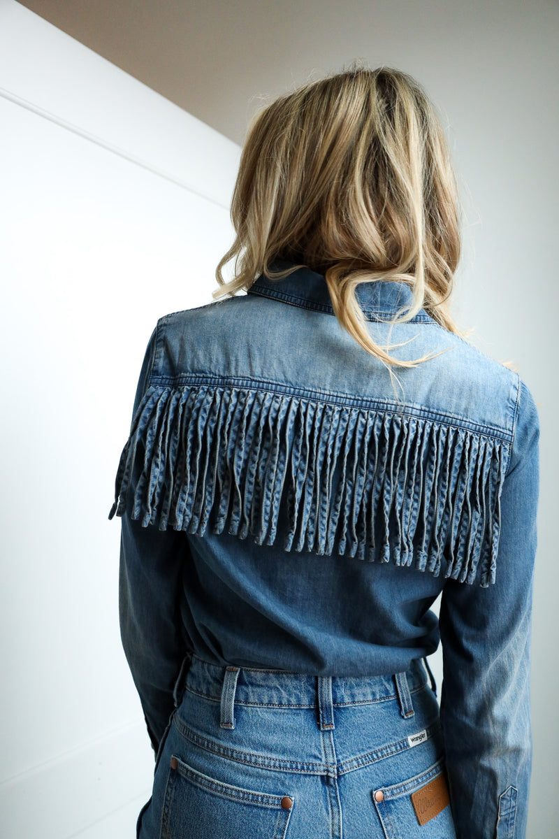 Person wearing a blue denim jacket with fringe details