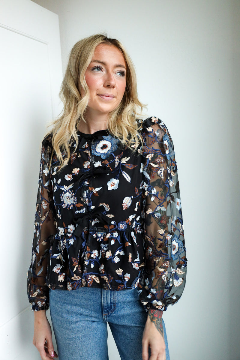Woman wearing a floral blouse with sheer sleeves against a plain background