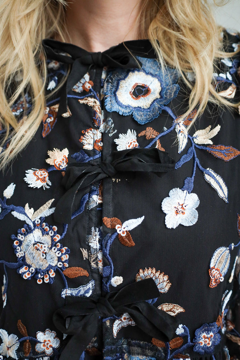 Close-up of a black floral embroidered blouse with a bow detail.
