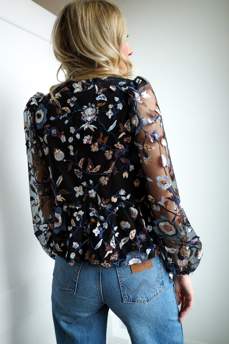 Person wearing a floral blouse and blue jeans against a plain background