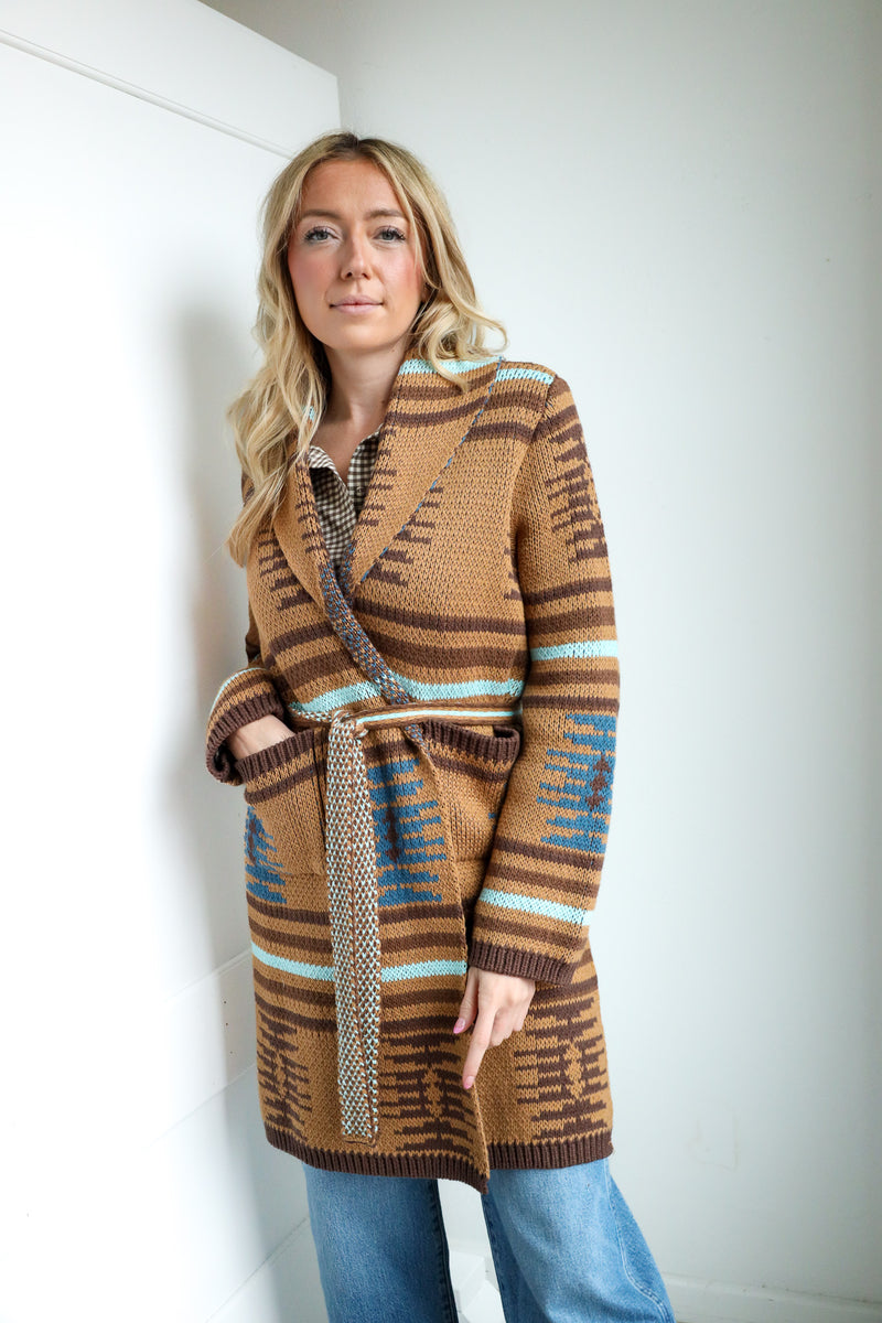 Woman wearing a patterned brown cardigan against a white wall