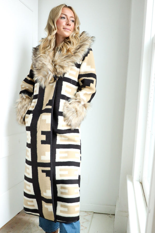 Woman wearing a long, patterned coat with fur trim indoors.