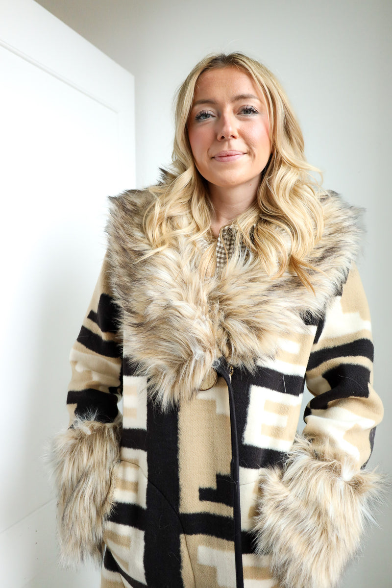 Woman wearing a patterned coat with fur trim against a white wall