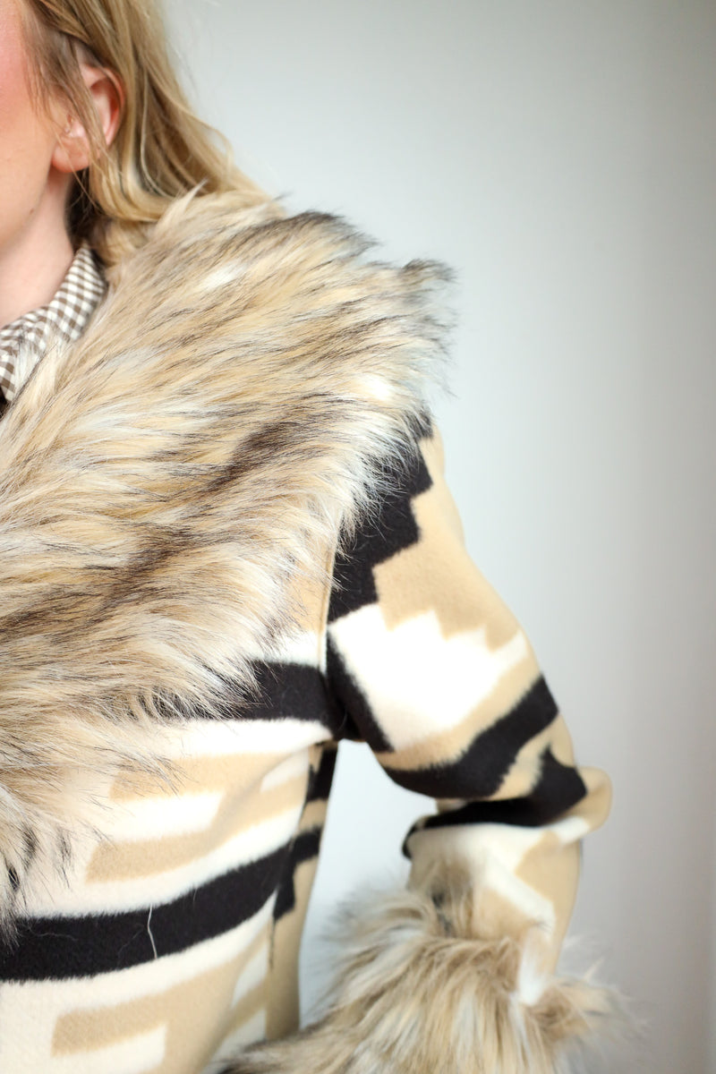Close-up of a person wearing a fur-trimmed coat with a neutral background