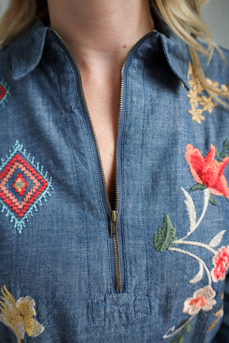 Close-up of a blue denim jacket with floral embroidery and a zipper.