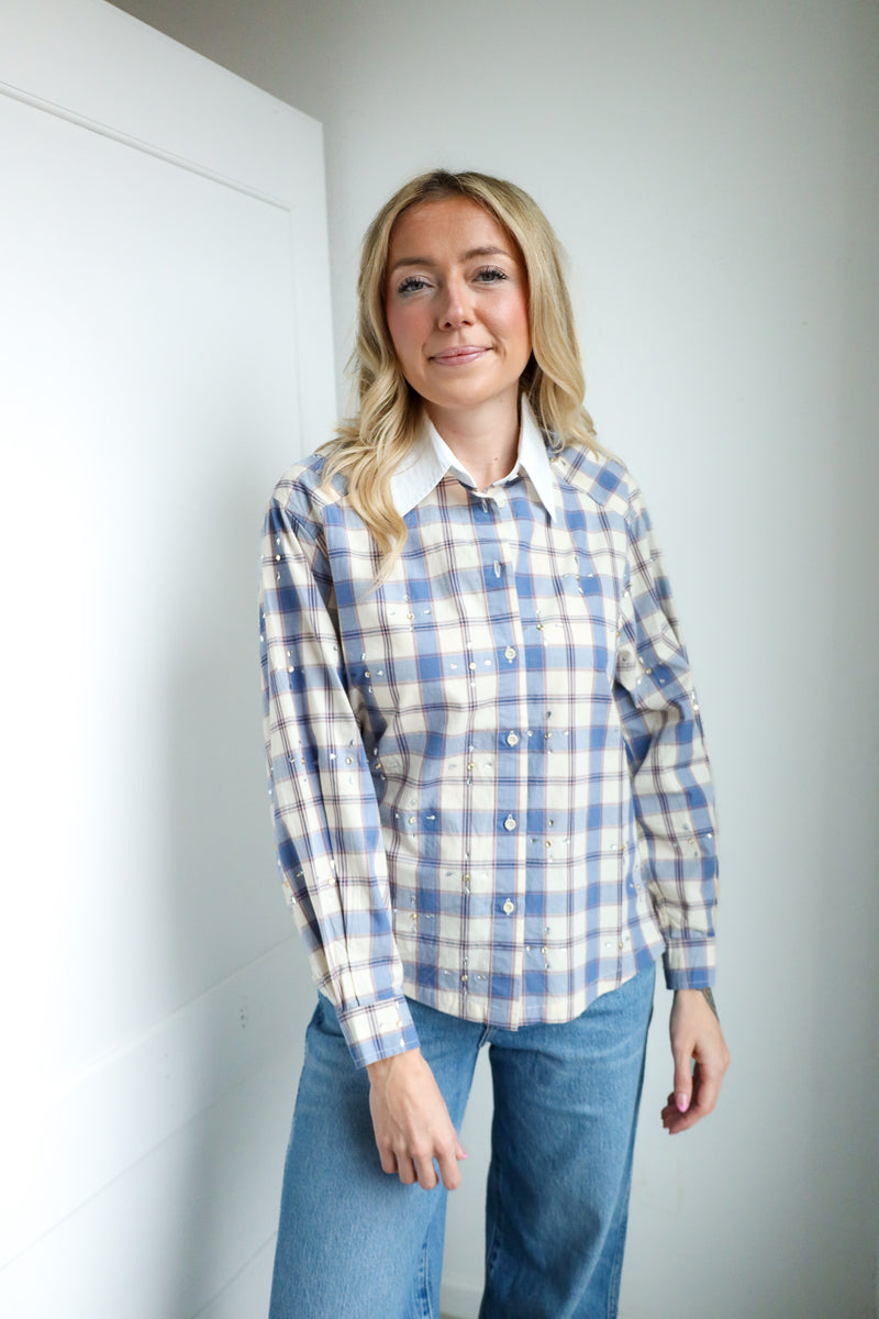 Woman wearing a blue and white plaid shirt with a white collar against a plain background