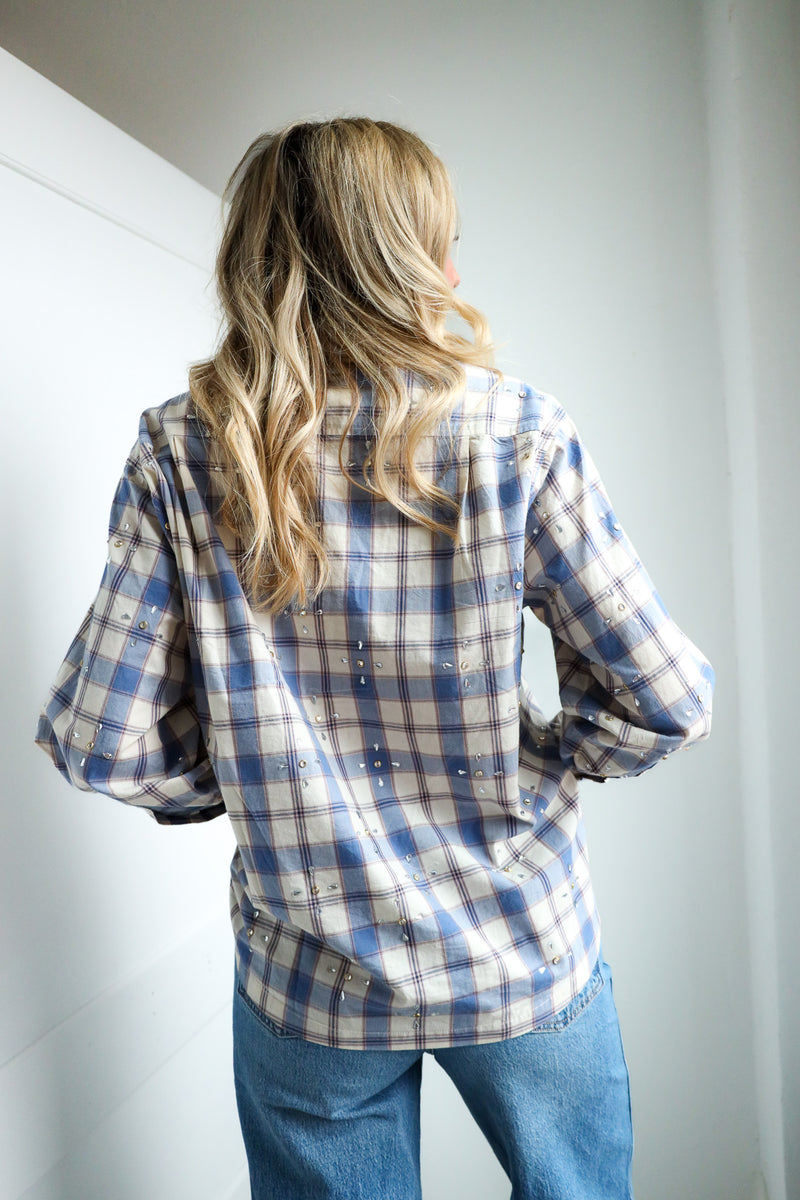 Person wearing a blue and white plaid shirt and jeans against a plain background