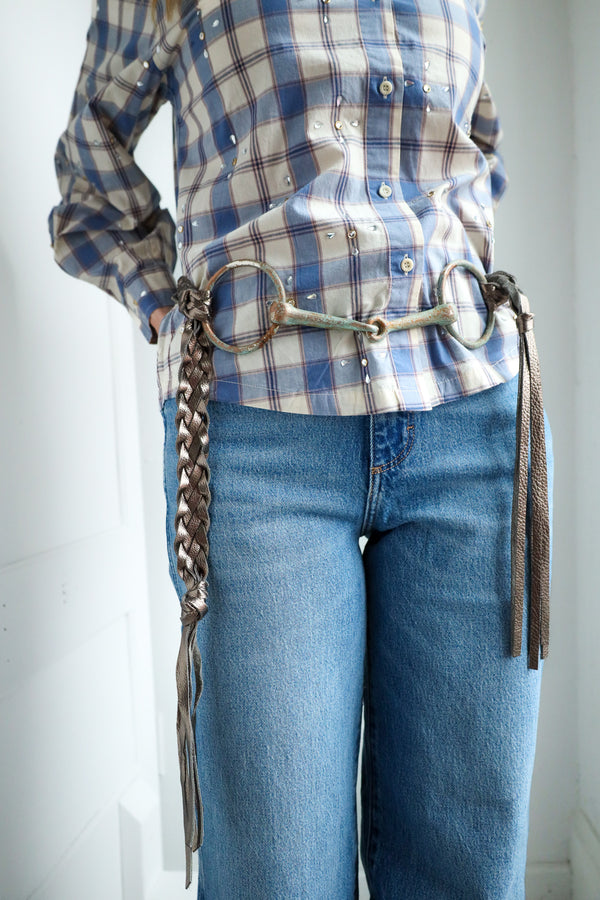 Person wearing a plaid shirt and blue jeans with a bridle over the shoulder against a white background