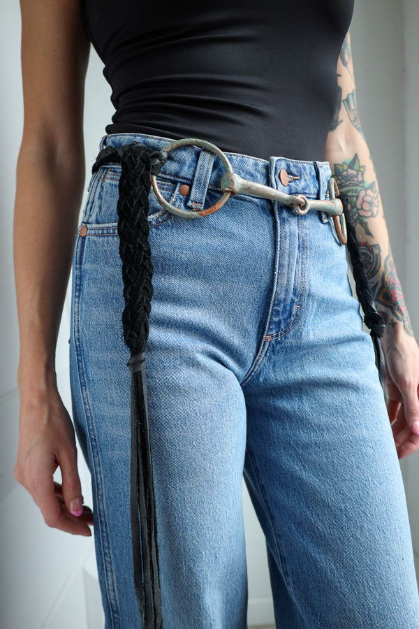 Person wearing blue jeans with a belt and black top against a neutral background