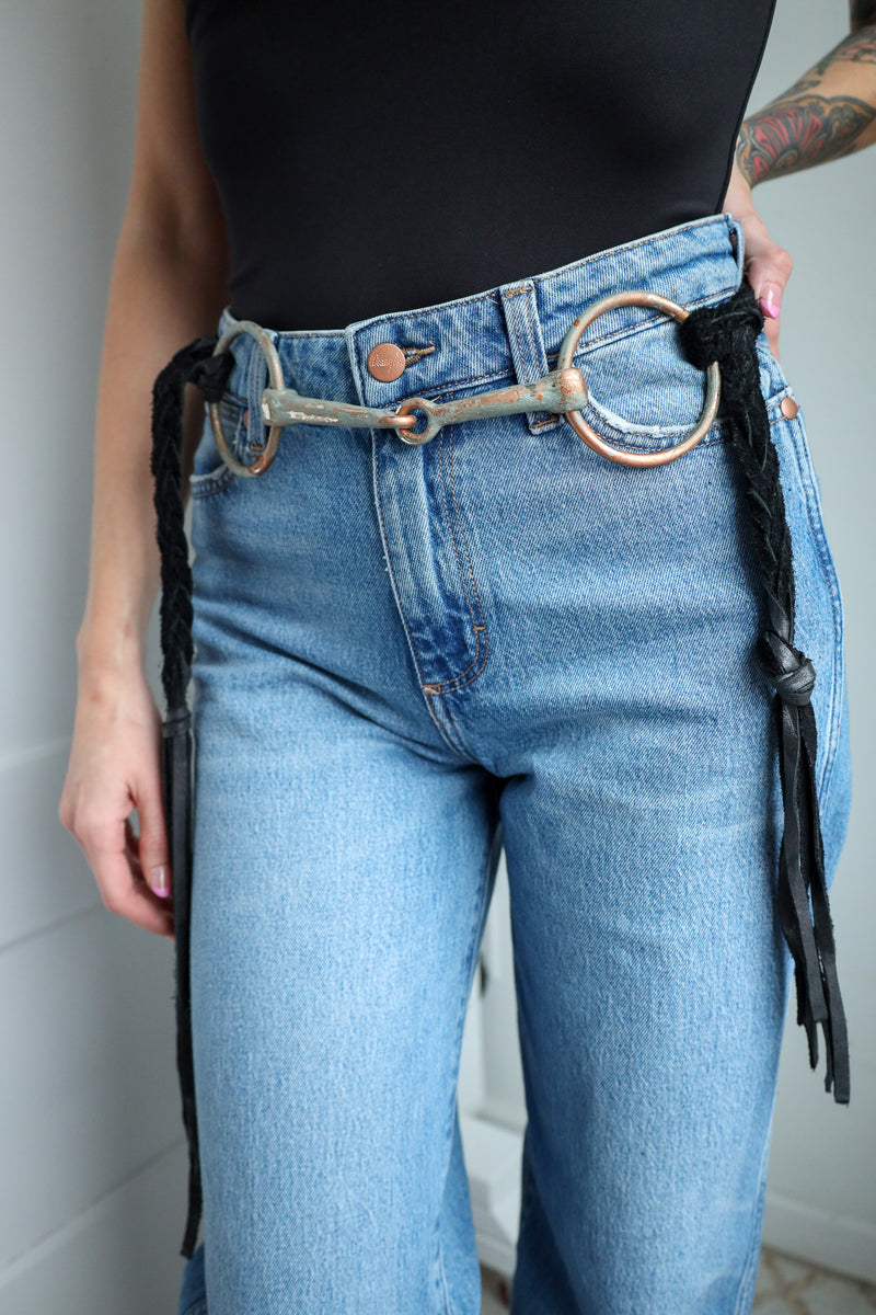 Person wearing blue jeans with a decorative belt featuring leather fringe.