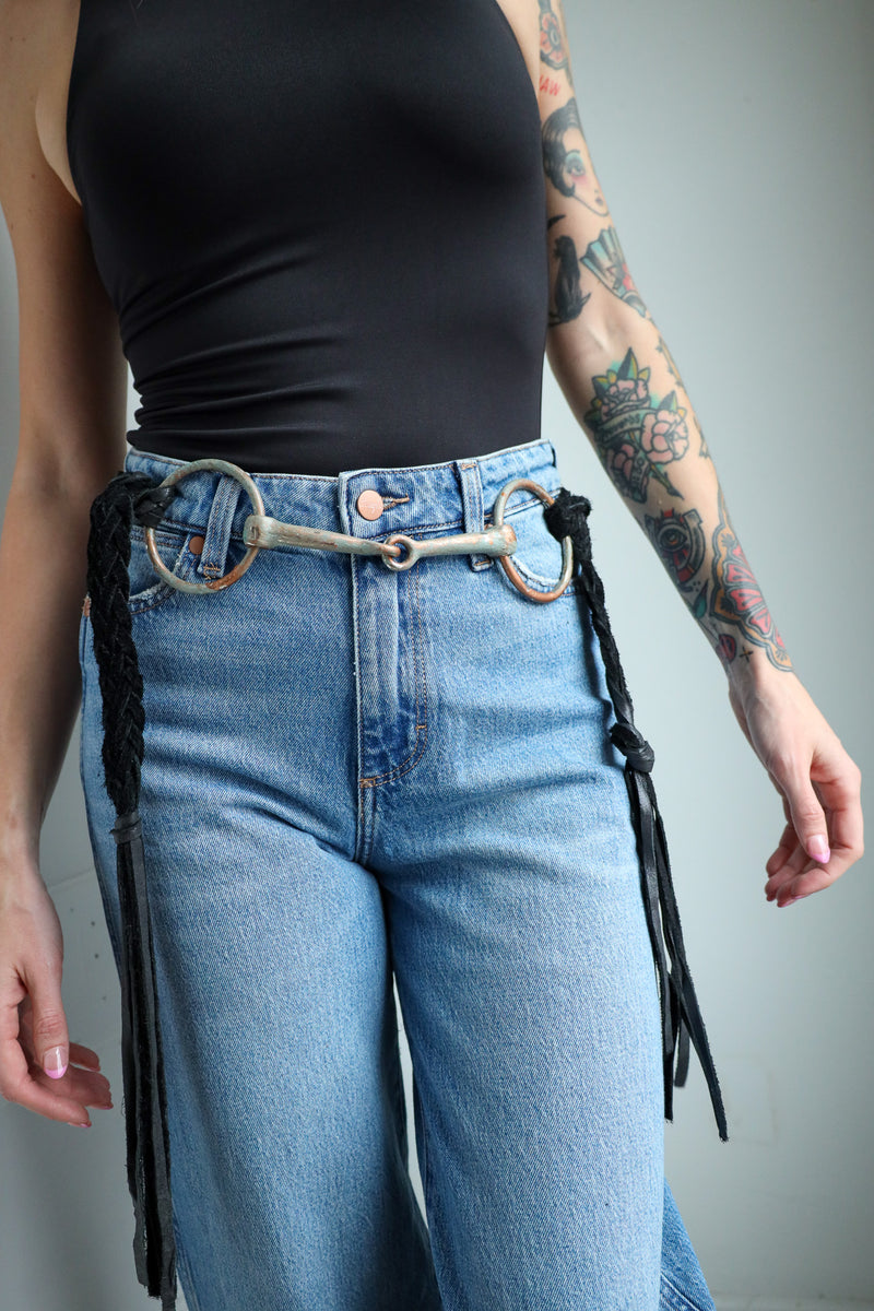 Person wearing blue jeans with a unique belt featuring a horse bit design on a gray background