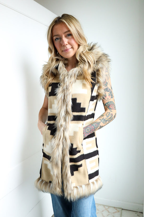 Woman wearing a patterned vest with fur trim indoors.