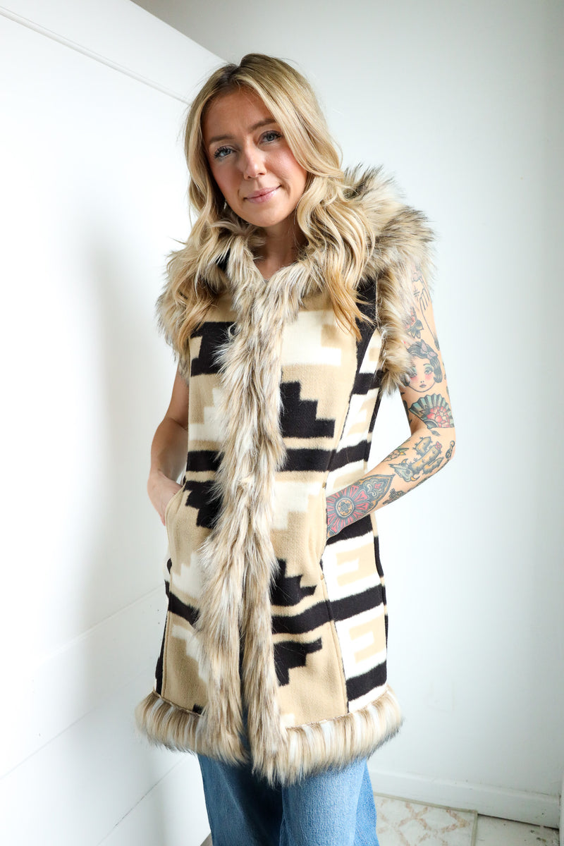 Woman wearing a patterned vest with fur trim indoors.