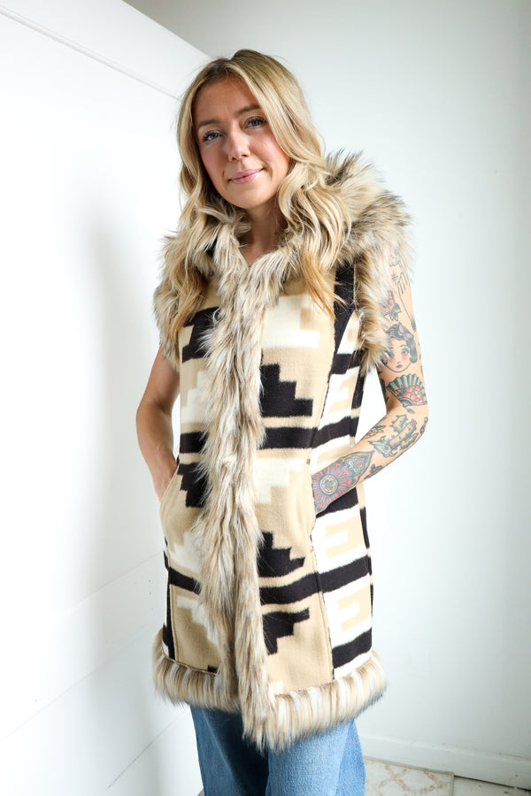 Woman wearing a patterned vest with fur trim against a white wall