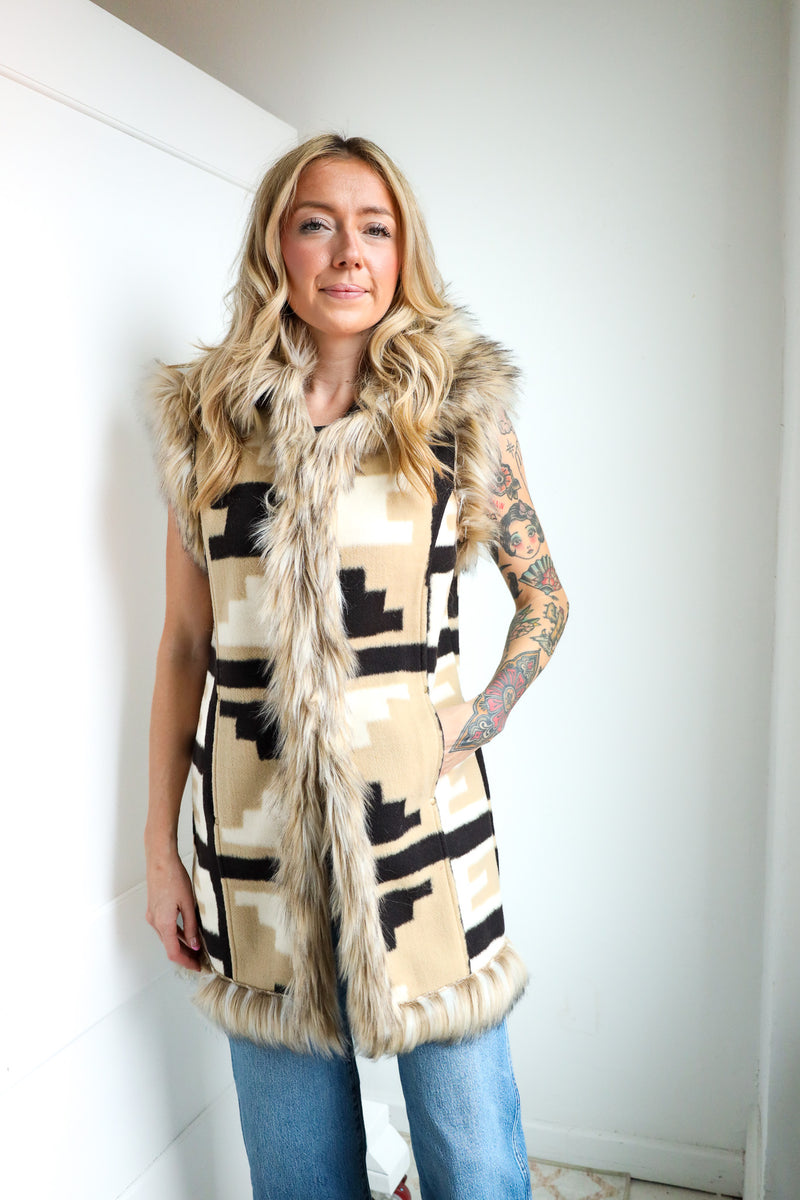 Woman wearing a patterned vest with fur trim against a white wall