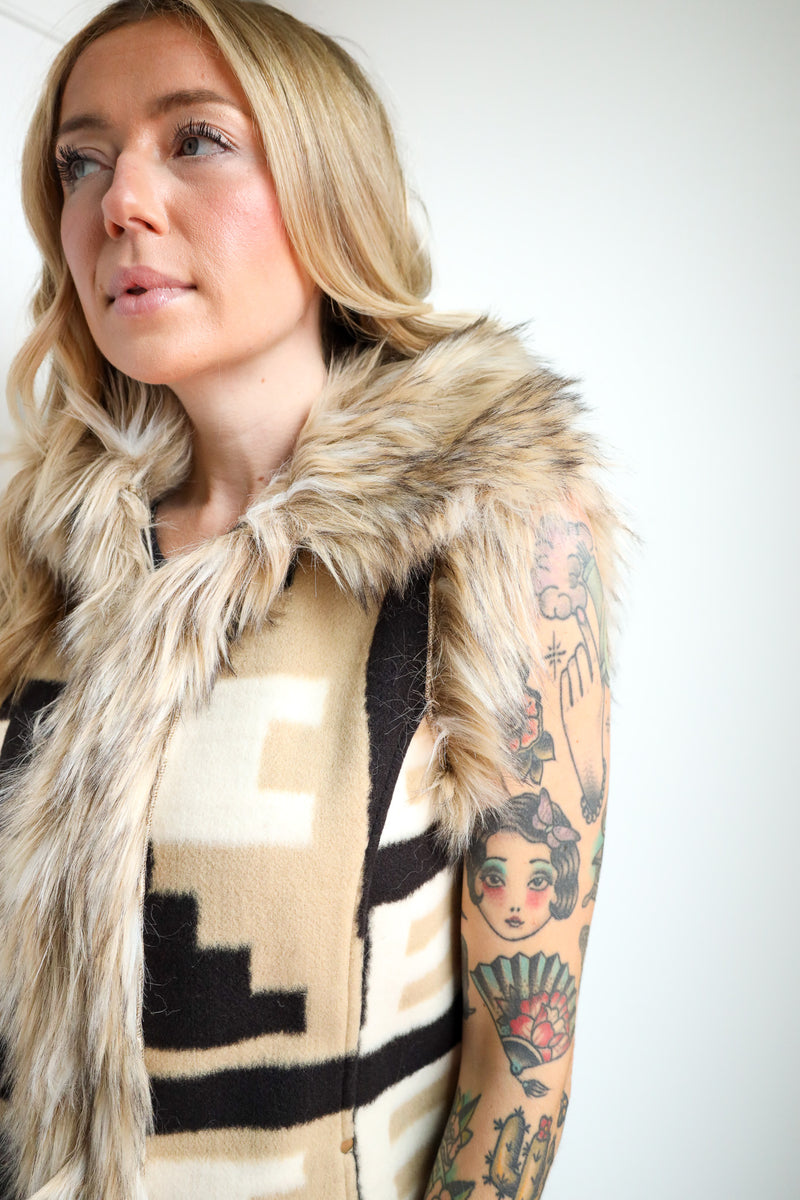 Woman wearing a patterned vest with a fur collar against a white background