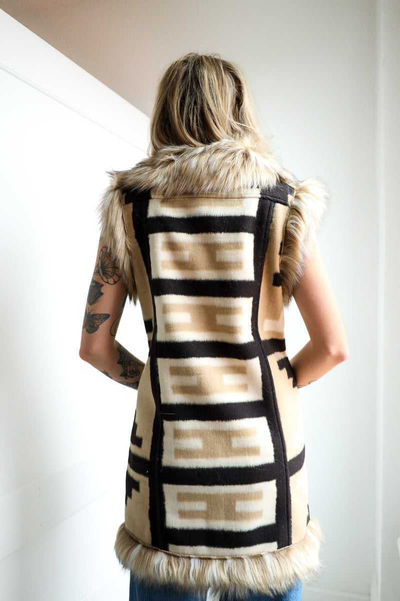 Person wearing a patterned vest with fur trim against a plain background