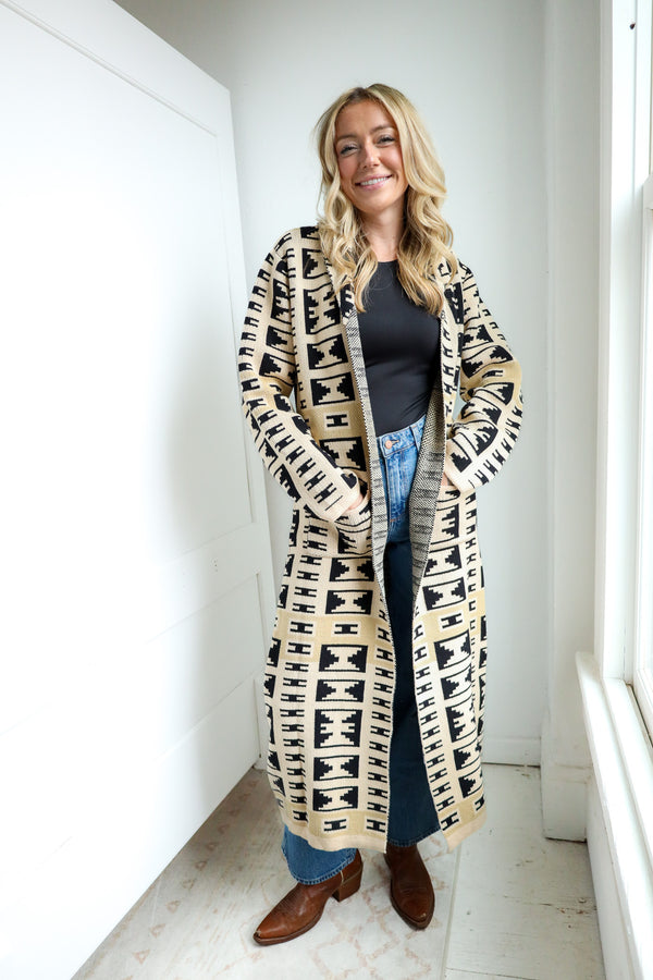 Woman wearing a long patterned cardigan in a minimal indoor setting