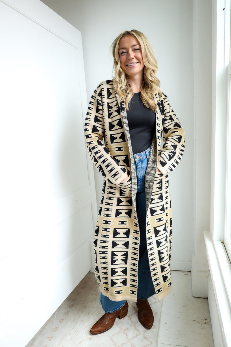 Woman wearing a long patterned cardigan in a minimal indoor setting