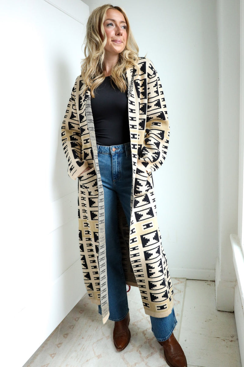 Woman wearing a long, patterned coat in a minimalistic room.