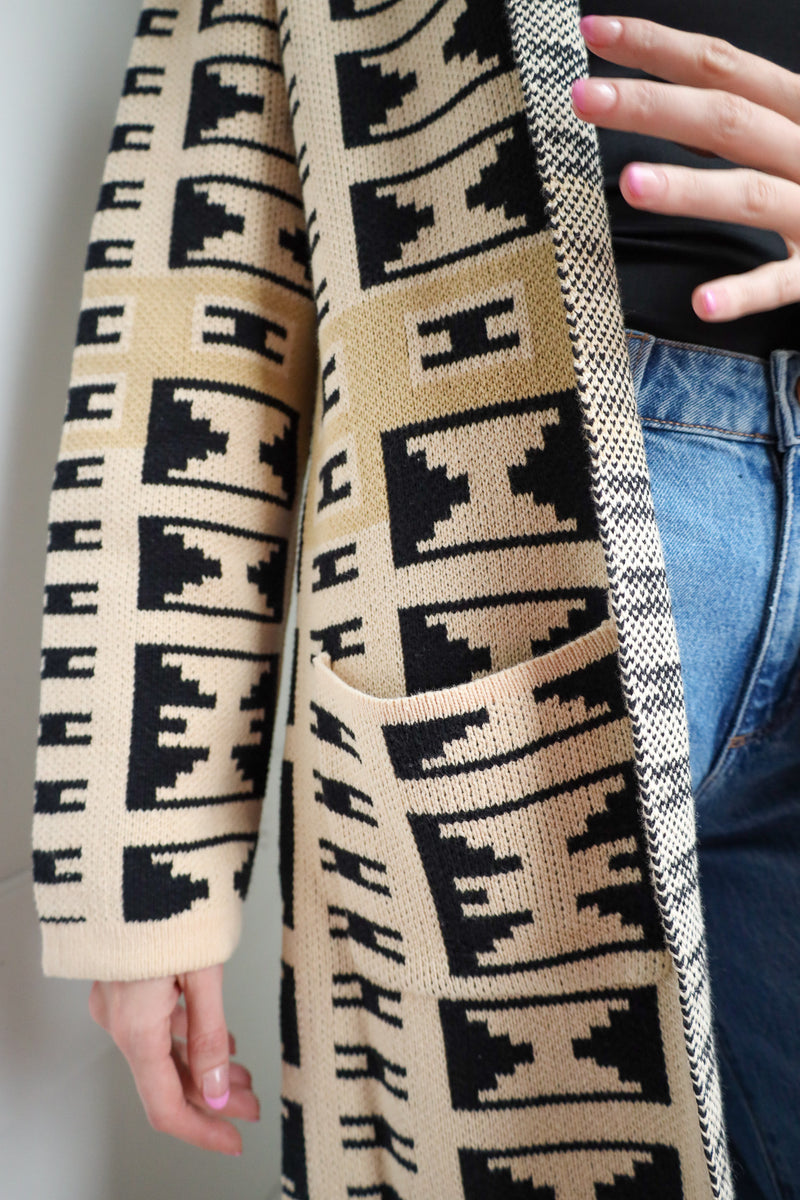 Patterned scarf with black and beige design held by a person wearing blue jeans.