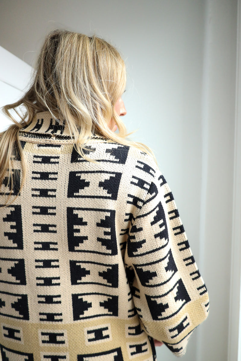 Person wearing a patterned beige and black cardigan against a plain background