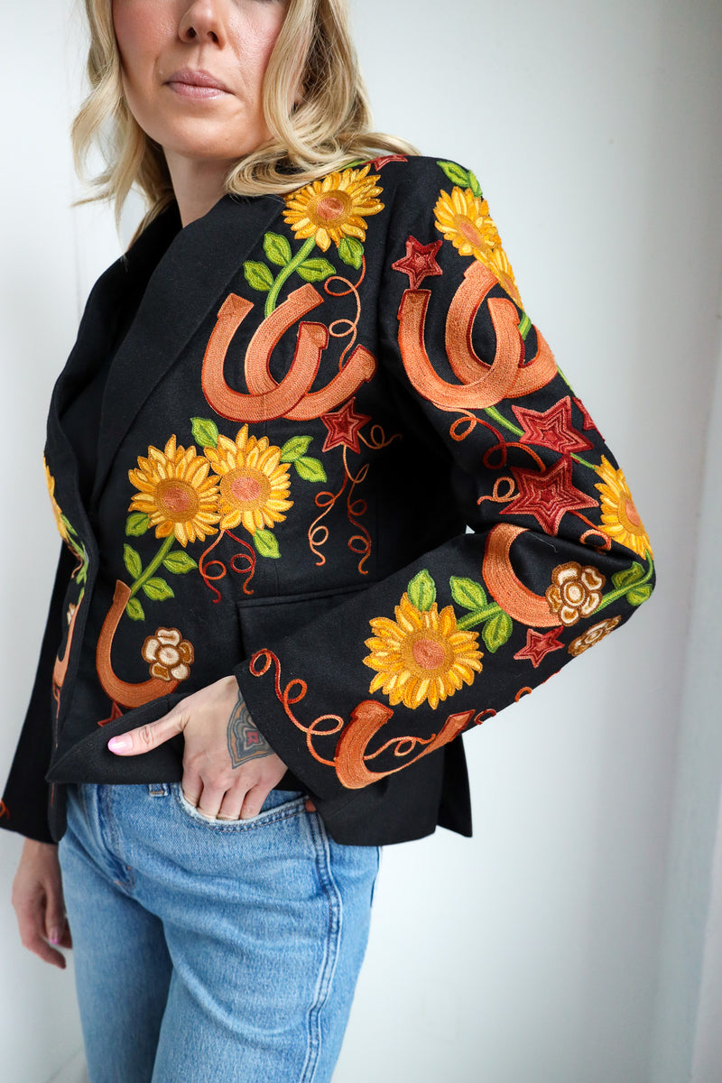 Woman wearing a black blazer with colorful floral and snake embroidery on a plain background