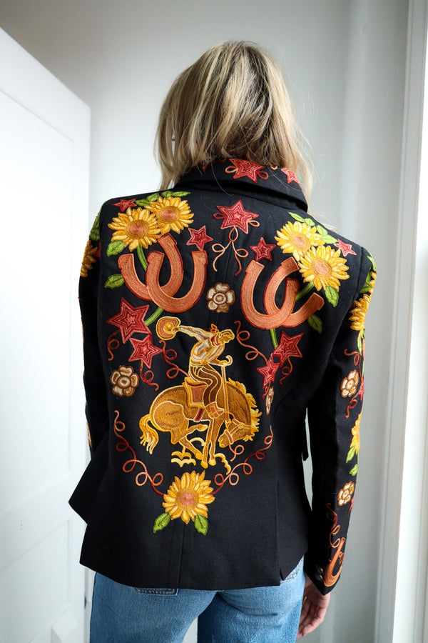 Person wearing a black jacket with colorful embroidered designs, including stars, flowers, and a horse rider.