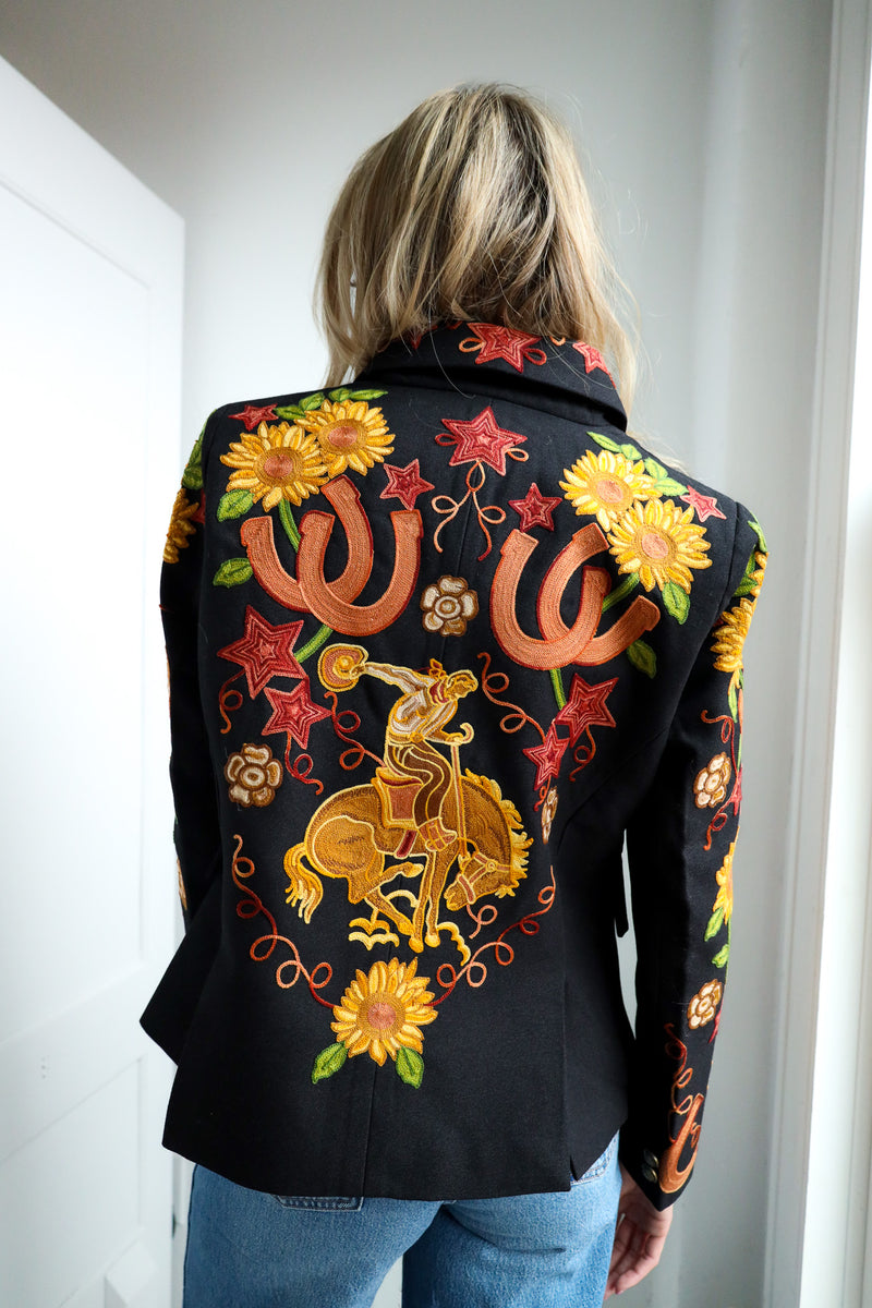 Person wearing a black jacket with colorful embroidered designs, including stars, flowers, and a horse rider.