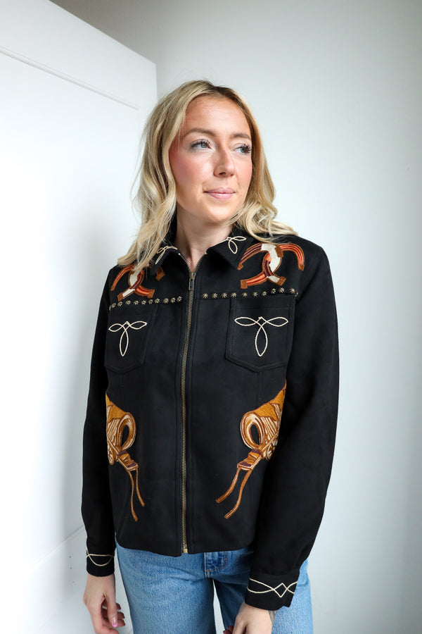 Woman wearing a black embroidered jacket with orange designs against a white background